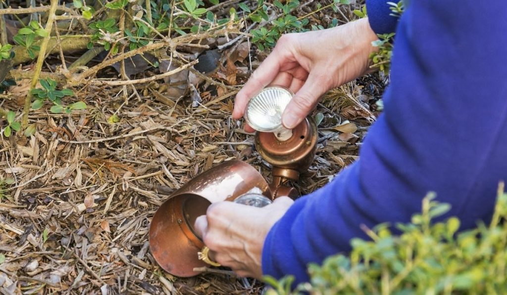 A homeowner changes a lightbulb in outdoor lighting