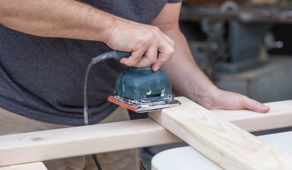 A man working on a home improvement project sanding wood with an electrical sander