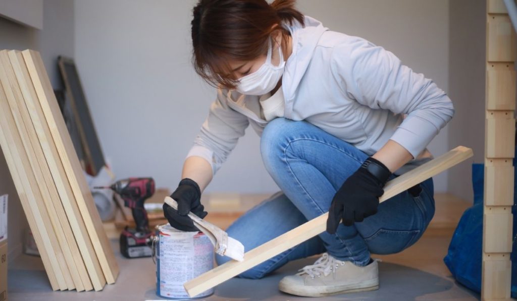 A woman painting lumber with a brush