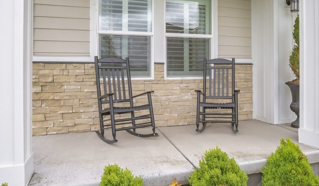 Rocking chairs against window at the porch of a home with wood and brick wall