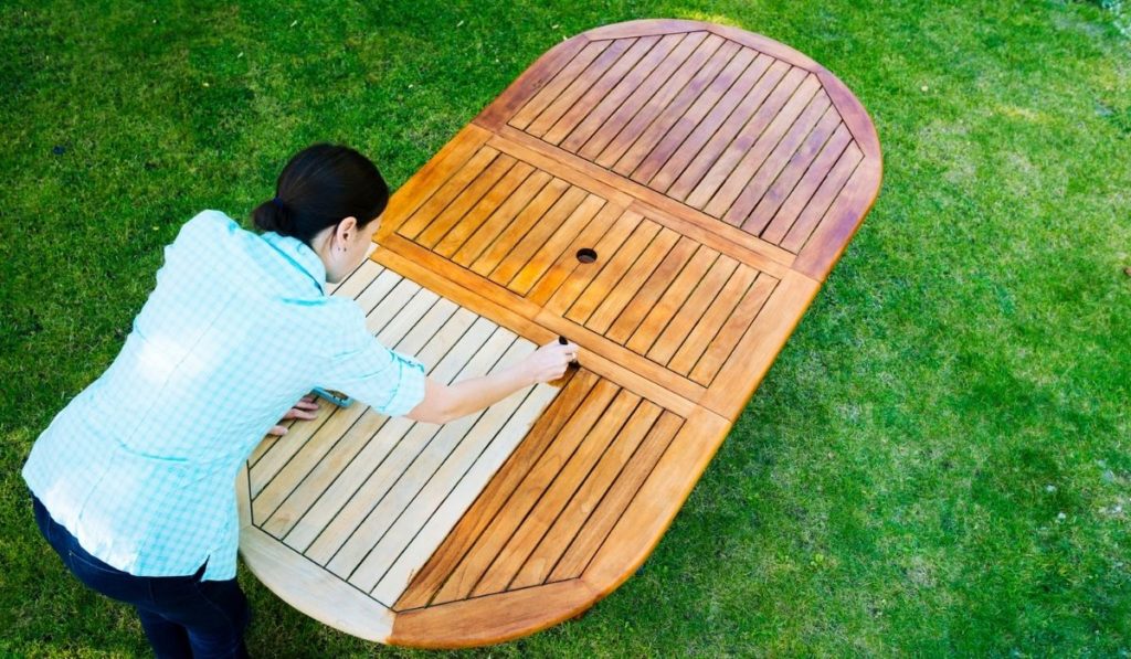 Woman painting wooden exotic wood table in the garden with a brush