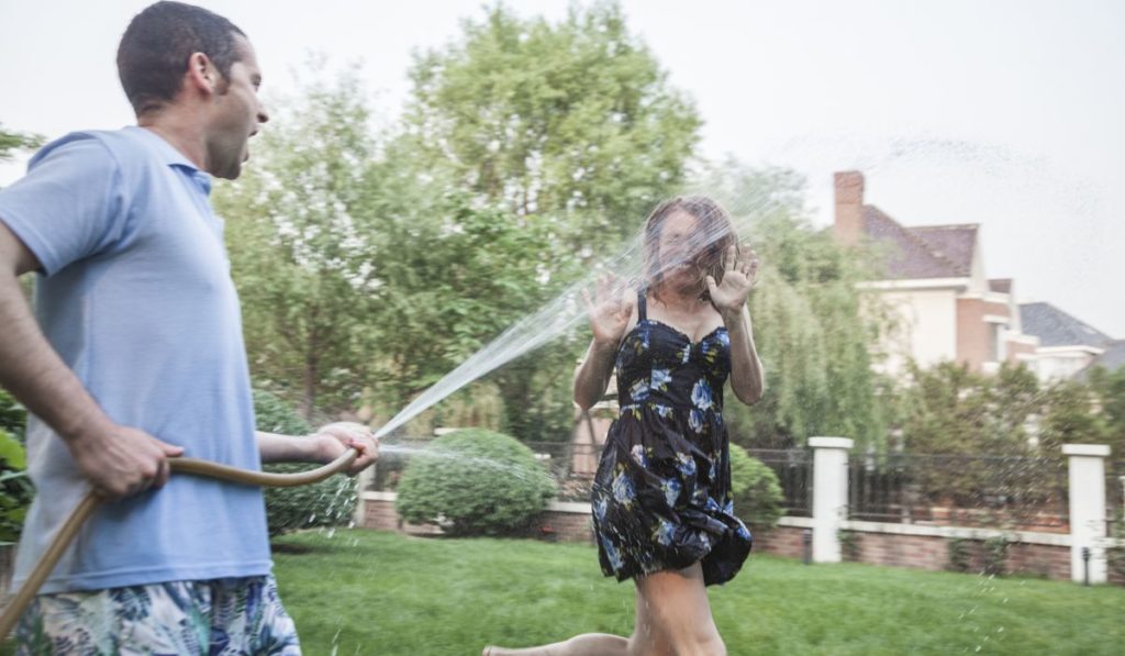 Couple playing with a garden hose and spraying each other outside in the garden