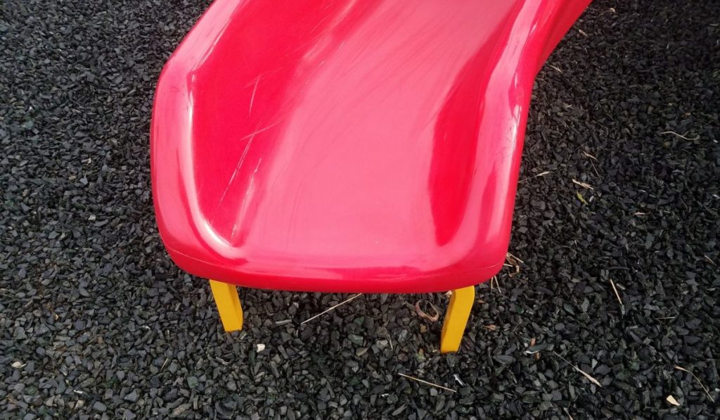 Red plastic slide with yellow metal and grey shredded recycled car tires