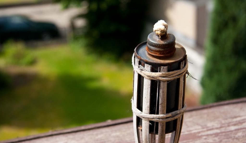 Closeup shot of tiki torch behind a field of grass and a car 