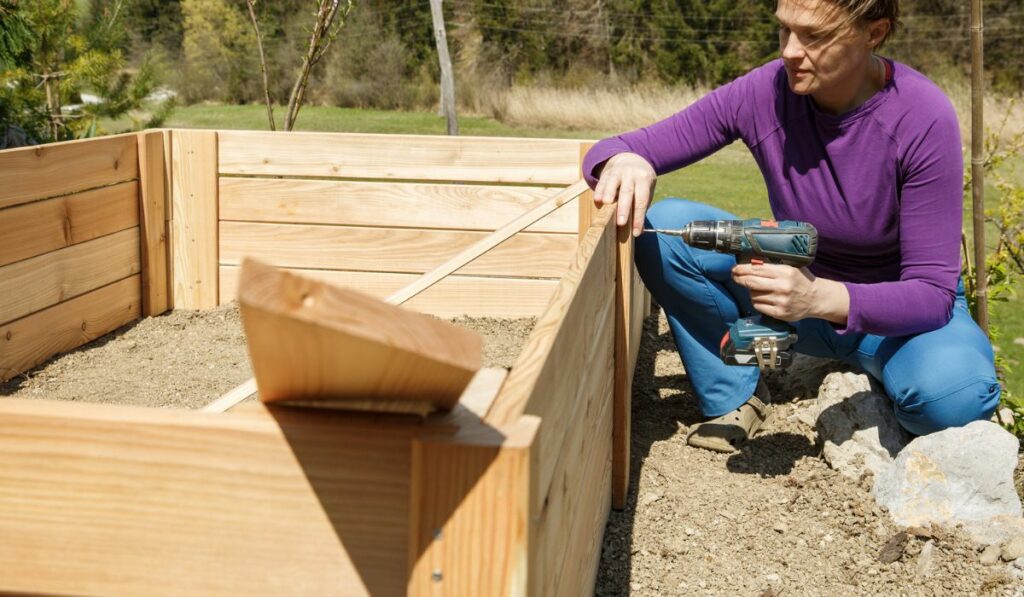 Woman screwing wooden frame for a raised garden bed
