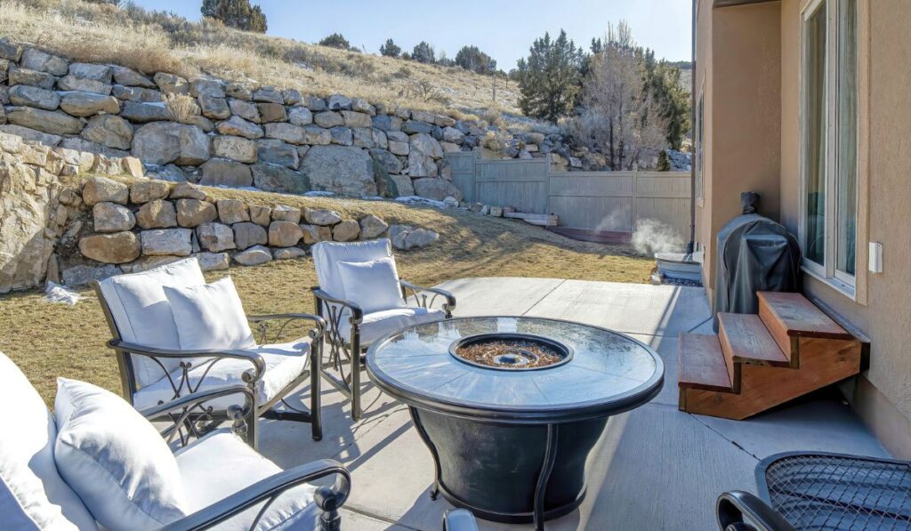 Pano Fire pit and paved patio at sunny backyard of house with stone retaining wall